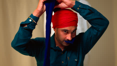 Fotografía-De-Estudio-De-Un-Hombre-Sikh-Mayor-Que-Ayuda-A-Un-Hombre-Sikh-Más-Joven-A-Atar-La-Tela-Para-Un-Turbante-Contra-Un-Fondo-Liso,-Filmada-En-Tiempo-Real-4